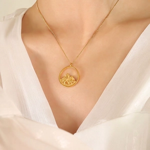 Elegant gold necklace with circular mountain pendant worn by a model on white background