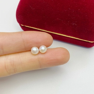 Close-up of white freshwater pearl earrings held in hand with red velvet jewelry box