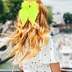 Fluorescent yellow bow hair clip worn by a woman with a scenic water town background