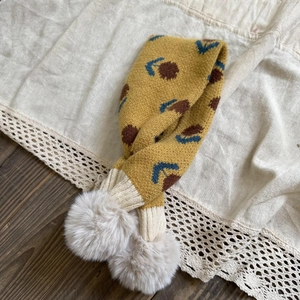Detail of yellow knit toddler scarf with floral patterns and beige faux fur pom-poms