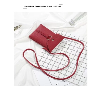 Detail of red litchi texture leather phone bag with golden ring buckle and slim strap