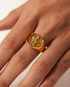 Close-up of a gold heart-shaped signet ring with angel relief on a finger
