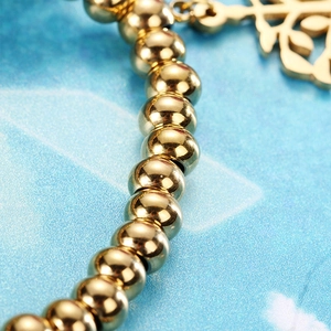 Vue macro d'un bracelet de perles dorées avec pendentif arbre de vie sur fond bleu
