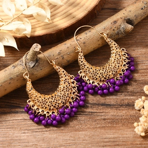 Boucles d'oreilles dorées avec pampilles de perles mauves sur fond de bois et fleurs