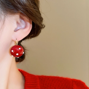 Detailed view of red mushroom-style polka dot earrings with gold hooks on a model