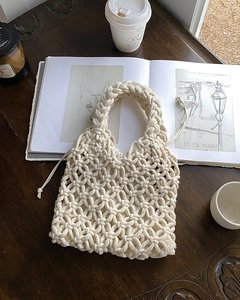 Artistic layout of a cream-white handmade knit handbag on a dark wooden table background