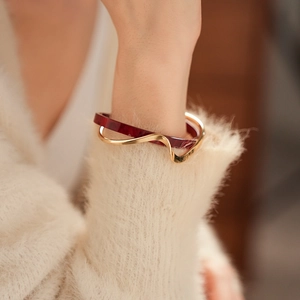 Detail of a double-layered gold bracelet featuring deep red marbled texture and wavy lines