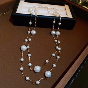 Detail of double-layer gold plated necklace with irregular white pearls on brown surface