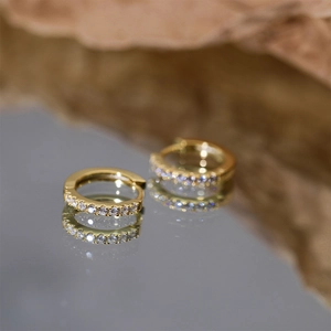 Macro shot of gold S925 sterling silver hoop earrings with small diamonds on mirror