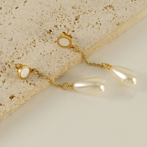 Vue détaillée des boucles d'oreilles dorées 18K avec perles sur une surface en pierre