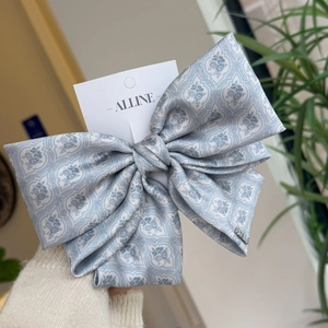 Detail of blue floral satin bow hair clip with vintage pattern and metal brand logo