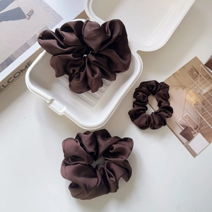 Close-up of three brown satin silk scrunchies with elegant folds on a white background