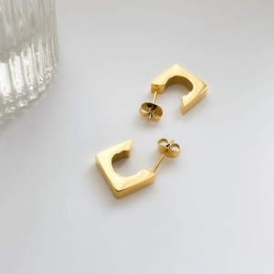 Polished 18K gold geometric square stud earrings shown in a minimalist studio setting