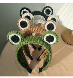 Close-up of cute knitted frog eye headbands in green, brown, white and black colors