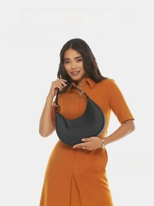 Detail of a minimalist black crescent moon handbag held by a model in an orange dress