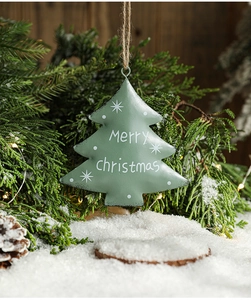 Detail of green tin Christmas tree ornament with Merry Christmas text on pine branch