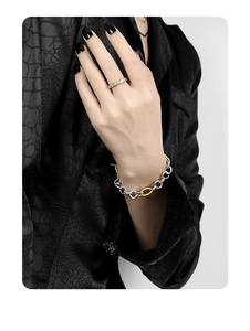 Close-up of two-tone silver and gold chain bracelet with OT buckle on leather jacket sleeve