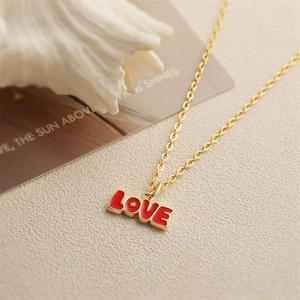 Collier vintage doré avec pendentif LOVE en émail rouge et tulipe sur un fond beige texturé