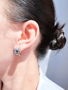 Close-up of a minimalist silver irregular C-shape earring on a model's ear with glossy finish