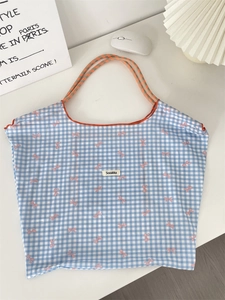 Detail of blue checkered tote bag with pink bows and vibrant orange trim accents