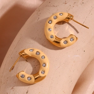 Detail of gold-plated C-shaped earrings with cream enamel and sparkling crystals