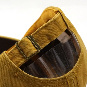 Detailed close-up of the adjustable bronze buckle and cotton label on a tan baseball cap