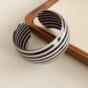 Detail of wide black and white striped cuff bracelet on a wooden tray with soft lighting