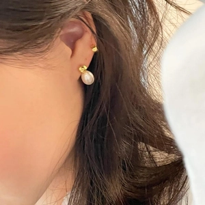 Detail of elegant white irregular pearl earrings with gold base worn by female model