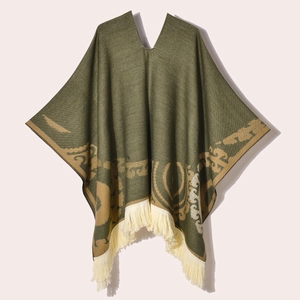 Detail of army green knitted poncho featuring ethnic patterns and beige tassel fringe