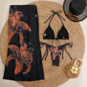 Flat lay of floral bikini set with mesh skirt on straw mat with beach accessories