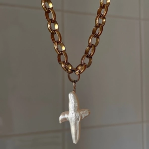 Vintage baroque pearl cross necklace with gold chunky chain displayed on a textured wall