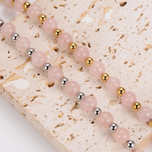 Pink quartz bead bracelet with gold and silver accents on a natural beige stone
