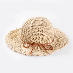 Détail du tissage du chapeau de paille beige avec bord ondulé et ruban marron
