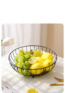 Close-up of black metal wire fruit bowl with fresh grapes and lemons on marble