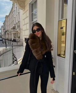 Detail of elegant black coat featuring a large brown faux fur collar and waist belt tie