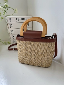 Detail of woven straw bucket bag with round wooden handle and brown leather trim accents