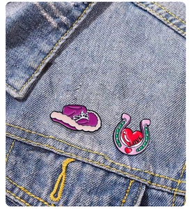 Détail de pin's émaillés avec fer à cheval cœur rose et chapeau de cowboy sur veste en jean