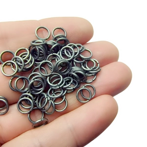 Handful of dark bronze jump rings for DIY jewelry making held in palm on white background