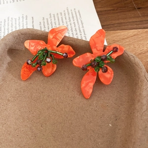 Detail of handmade orange flower stud earrings with green beads on a rustic ceramic tray