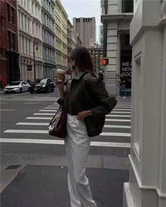 Stile street di una donna con giacca in similpelle vintage ampia e pantaloni larghi bianchi