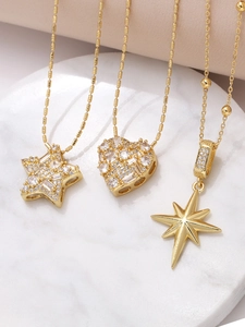 Close-up of gold-plated necklaces with zircon-studded heart and star pendants on marble
