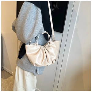 Close-up of beige ruched cloud bag featuring a round handle and slim leather shoulder strap