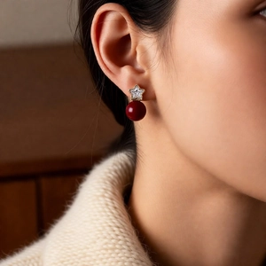 Detail of star-shaped 18K gold earrings with deep red pearl on model in soft lighting