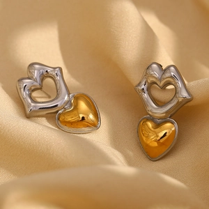 Detail of two-tone heart dangle earrings in gold and silver finish on silk fabric