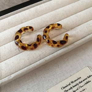 Detailed close-up of amber leopard print C-hoop earrings in a white velvet jewelry box