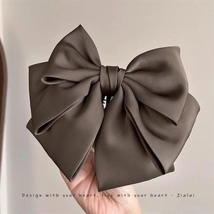 Detail of a large dark brown satin bow banana clip held by hand against a beige wall
