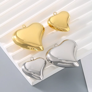 Polished hollow heart charms in gold and silver finishes in two sizes on a white board
