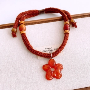 Detail of hand-woven orange cord necklace with floral resin pendant and wooden beads