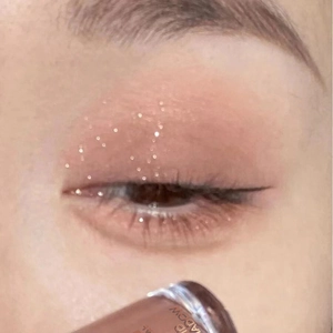 Close-up of sparkling pink-orange liquid eyeshadow with fine shimmer on eyelids