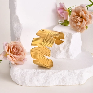 Close-up of golden leaf cuff bracelet with pink roses on white stone background
